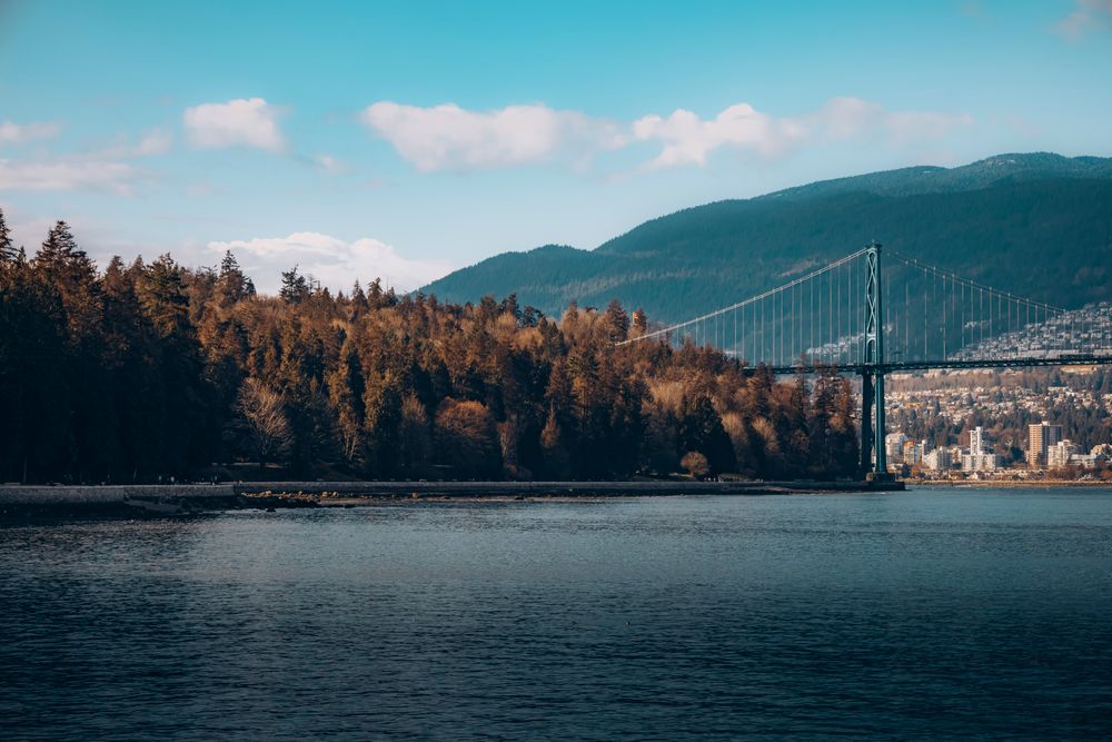 Lions Gate bridge over river into forest, Vancouver city and mountain in background