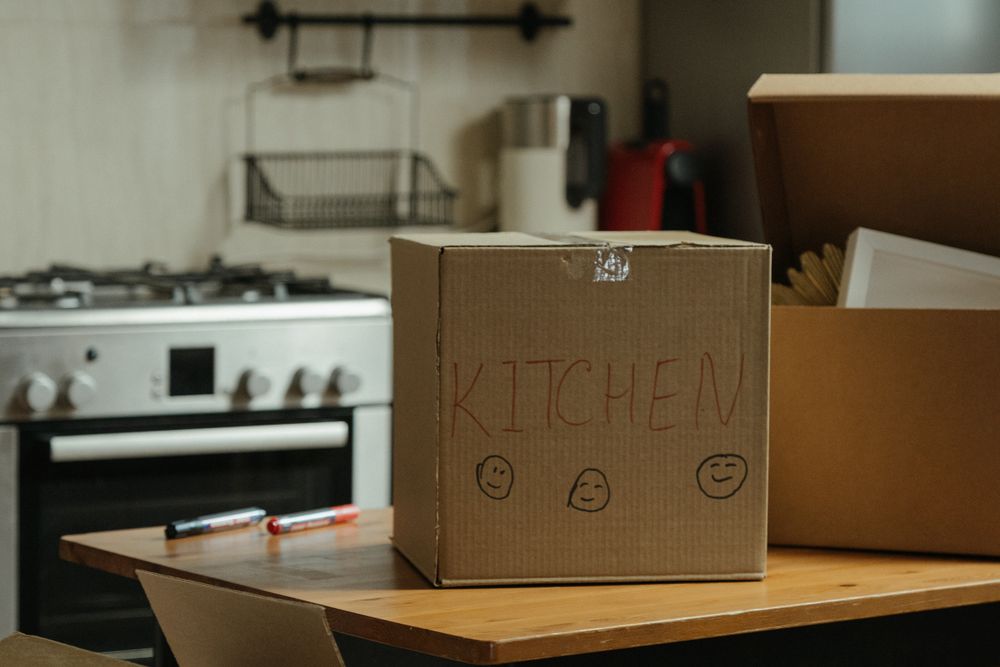 Brown cardboard box on white stove range with the word “Kitchen” written on it with red marker.