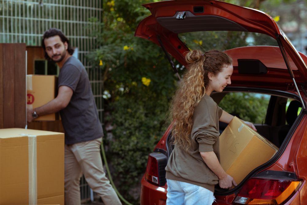 Couple getting carton boxes out of red car while relocating into a new home.