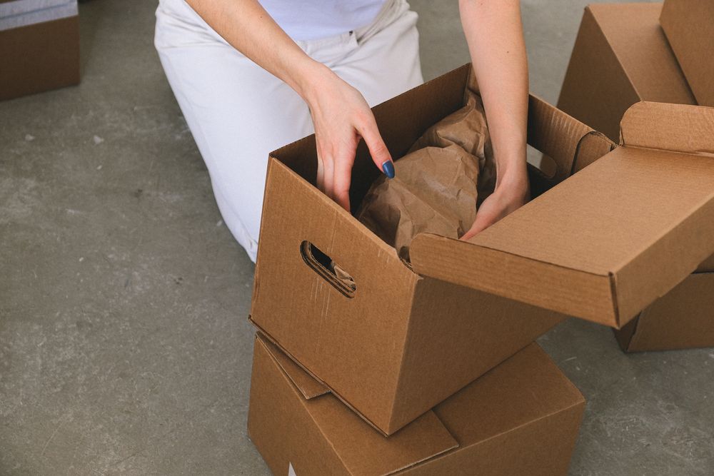 Faceless woman packing belongings into cardboard boxes.