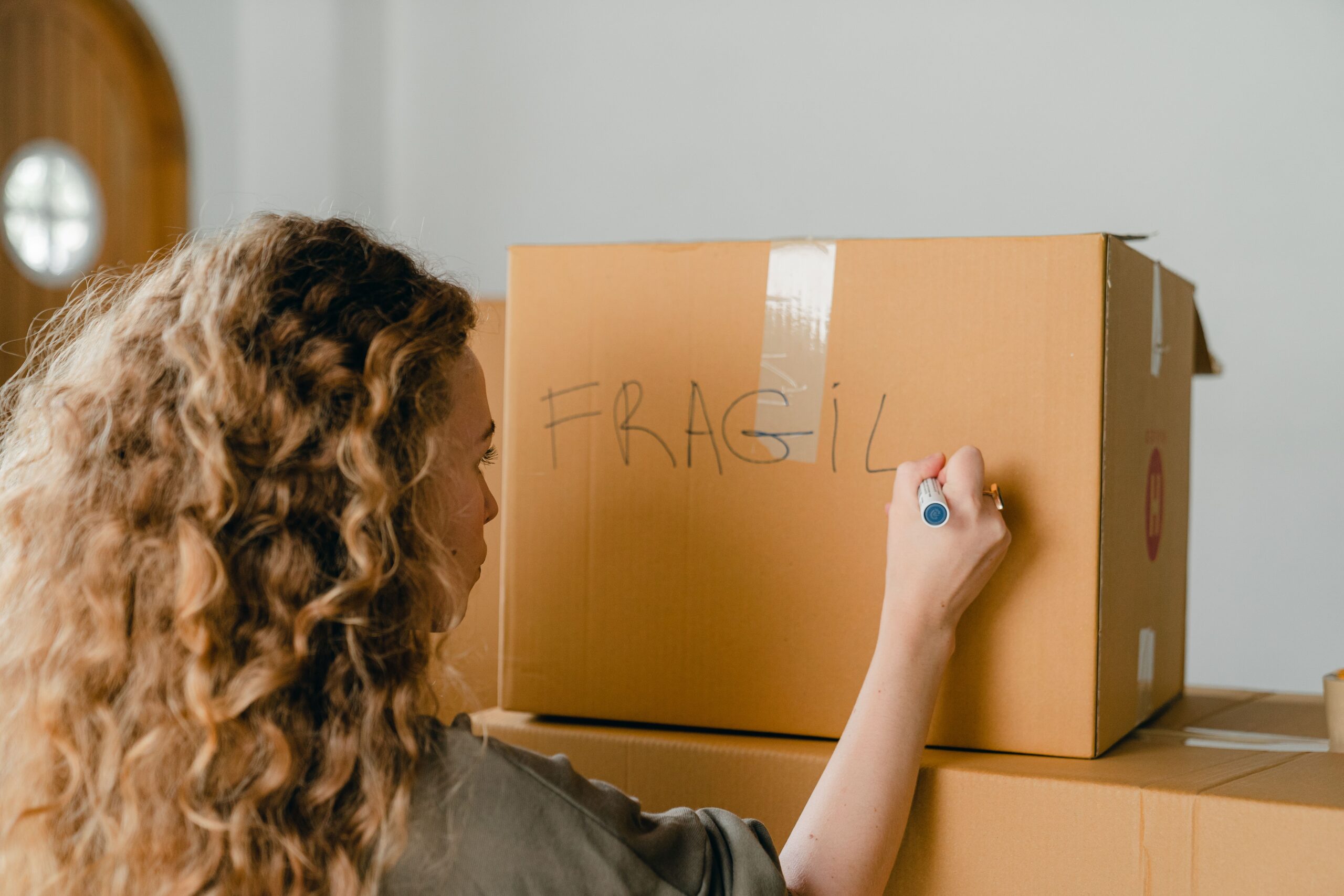 Unrecognizable woman writing “FRAGILE” note on carton box with marker.